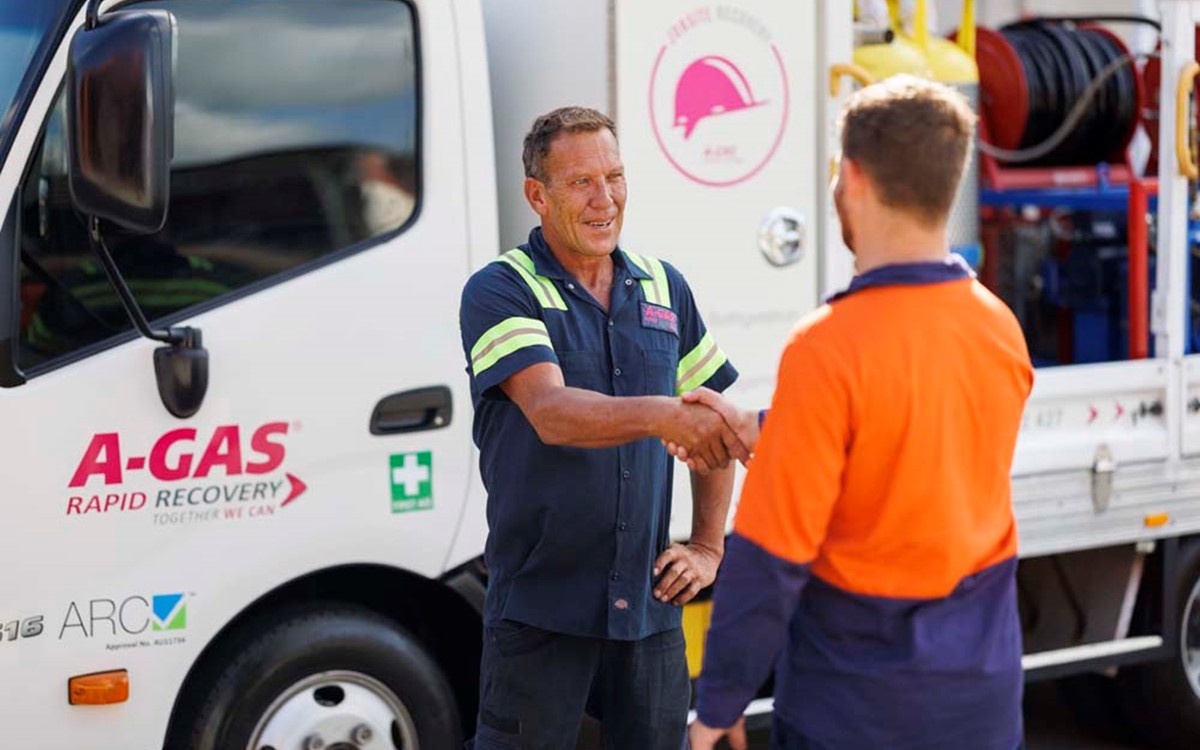 Two men shaking hands next to a white recovery truck