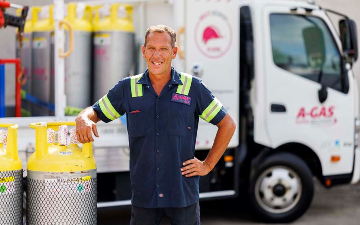 Man leaning against a cylinder in front of a white truck while smiling at the camera 