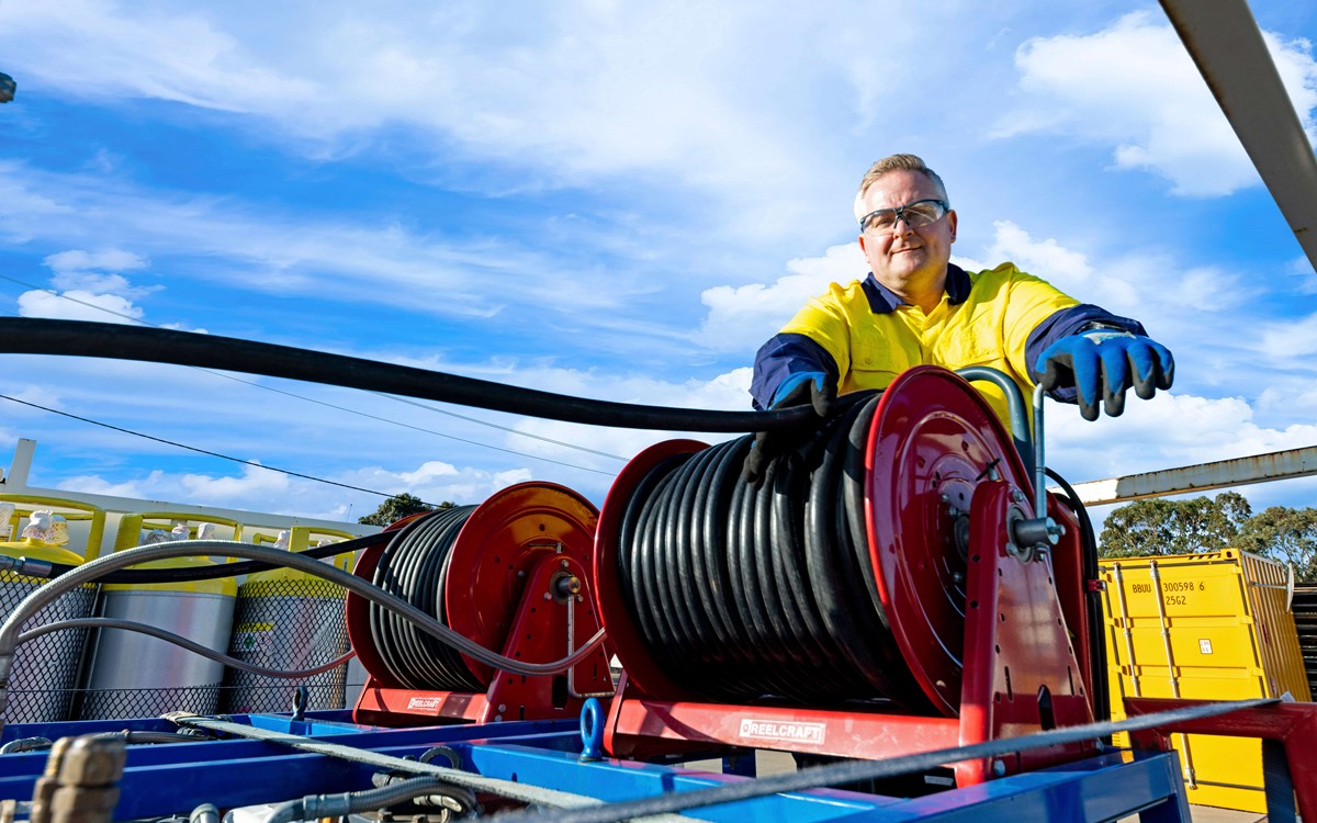Man working with black hose on the back of a recovery truck while smiling at the camera