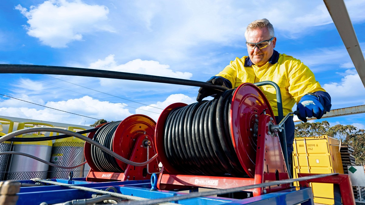 Man working with black hose on the back of a recovery truck 