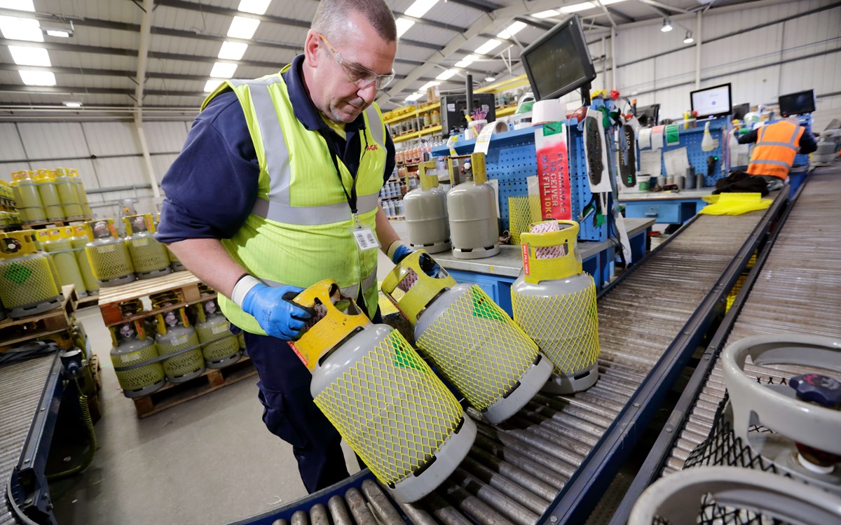 A man working in a warehouse, he is wearing a hi vis jacket and moving gas cylinders