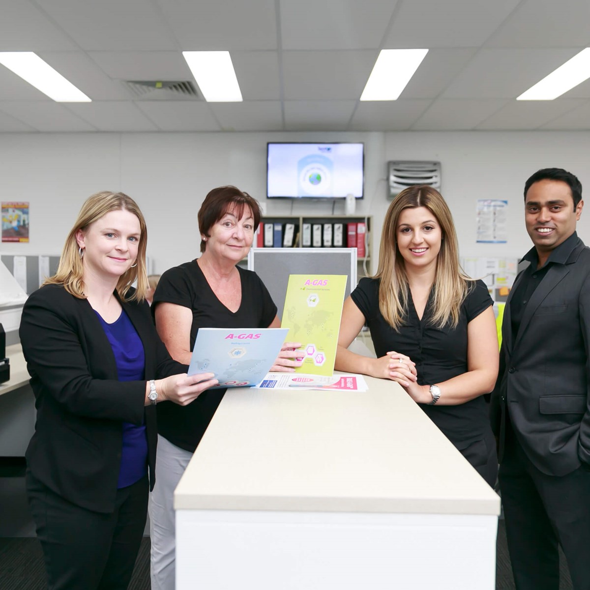 four workers in office environment looking at camera and smiling