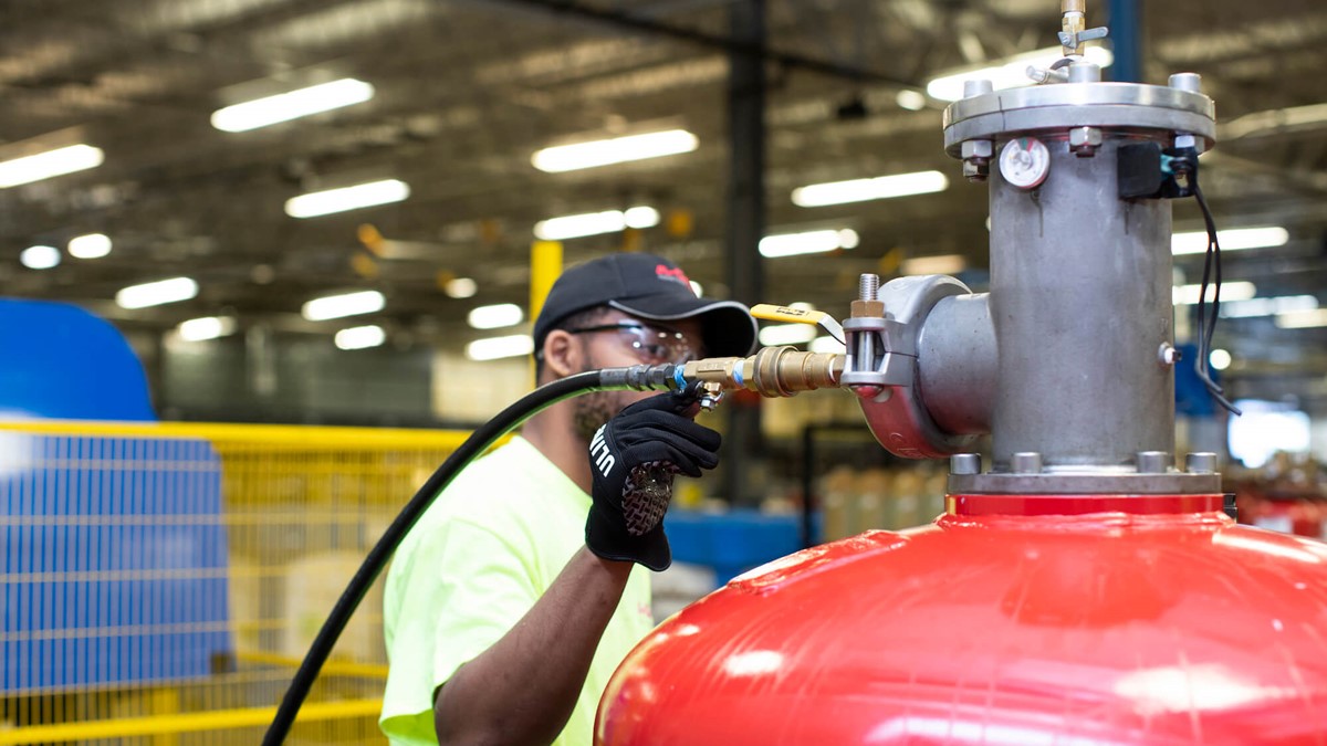 A man working on a large red cylinder inside a warehouse