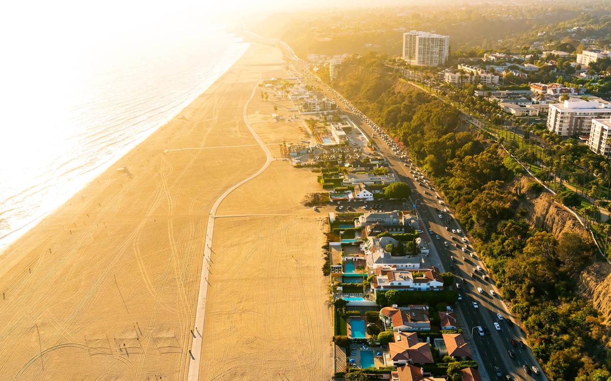A birds eye view of Santa Monica beach in California. A row of buildings swimming pools stretch along the sandy beach into the distance.