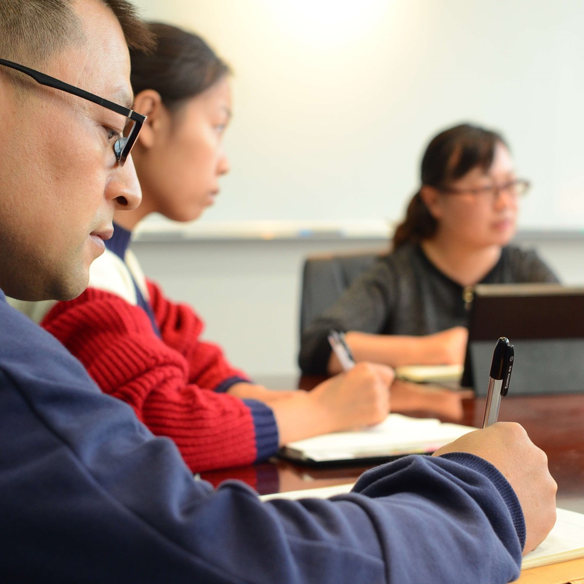 Close up of a man in a meeting, there are other people visible in the background