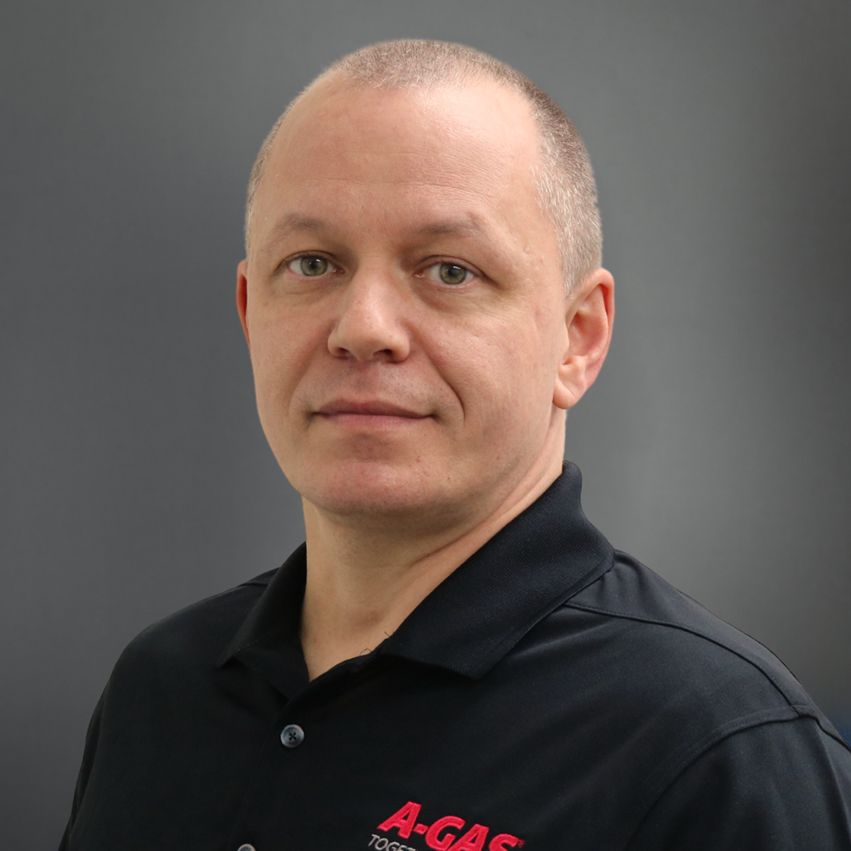 A man in a navy blue polo with the pink A-Gas looks at the camera 