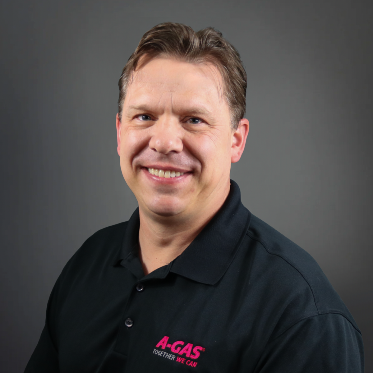 A man in a black polo with the pink A-Gas logo smiles at the camera 