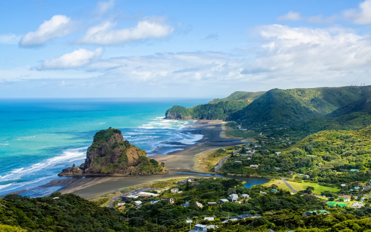 A wide angle shot of mountains in New Zealand with the beach in the background of the image, meeting the bottom of the mountains