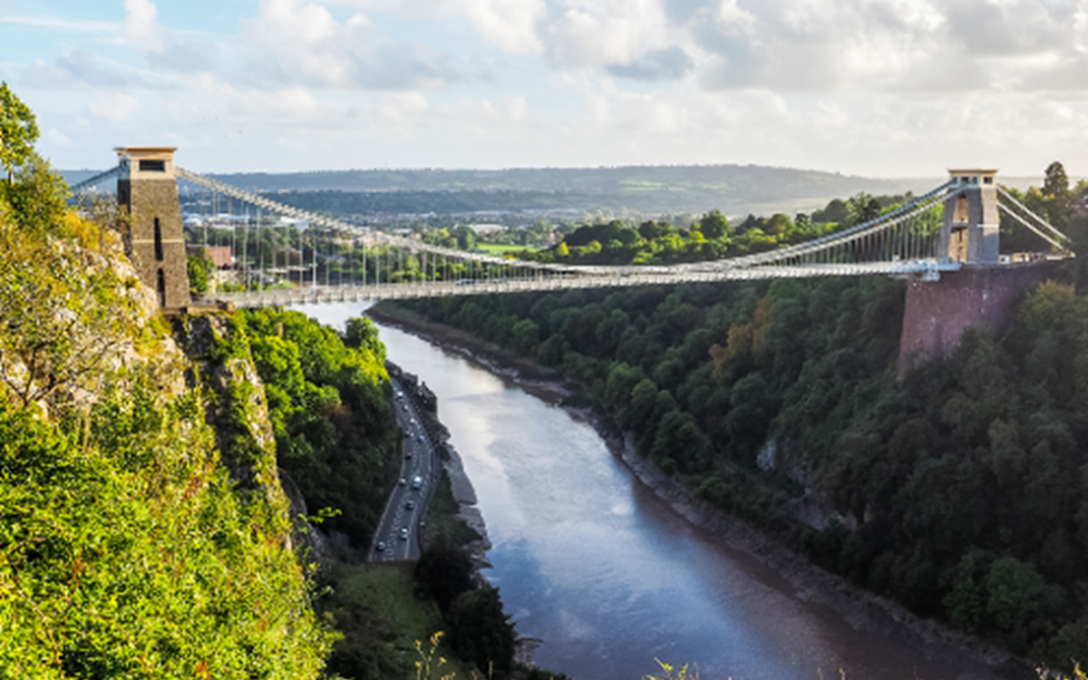 An image of Clifton Suspension Bridge with green trees and bushing around it