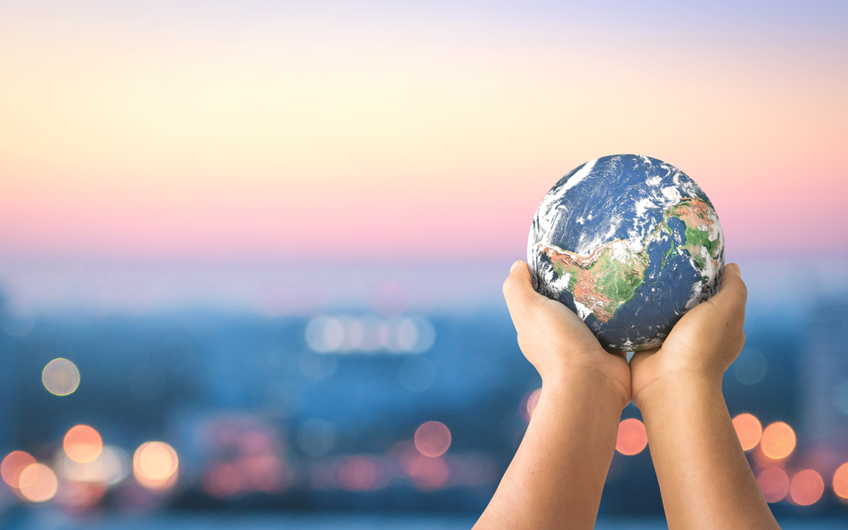 A pair of hands hold a model of the globe against a blurred background of city lights at sunset