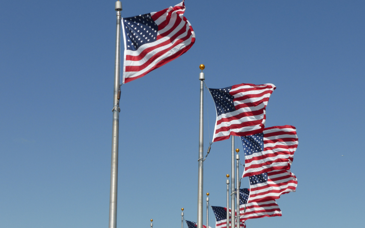 A row of USA flags outside on poles against a pale blue sky 